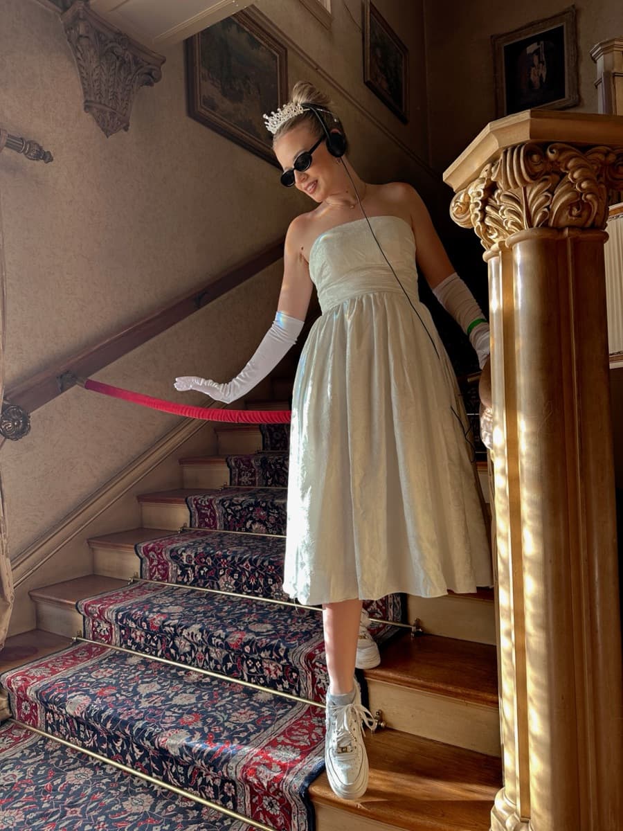 Kayla in a tiara and white gloves on a grand staircase at the Princess Diaries pop-up