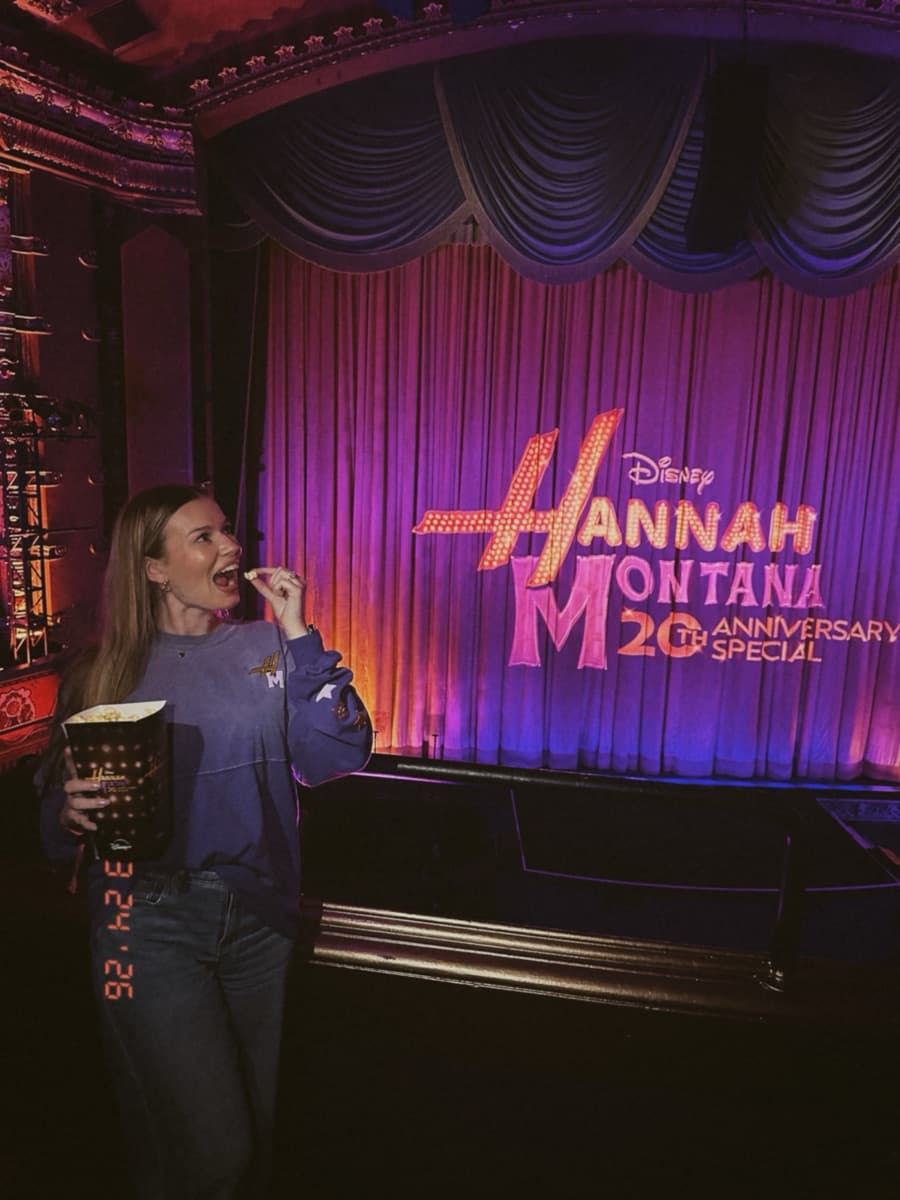 Kayla in front of the Hannah Montana 20th Anniversary Special title on the stage curtain
