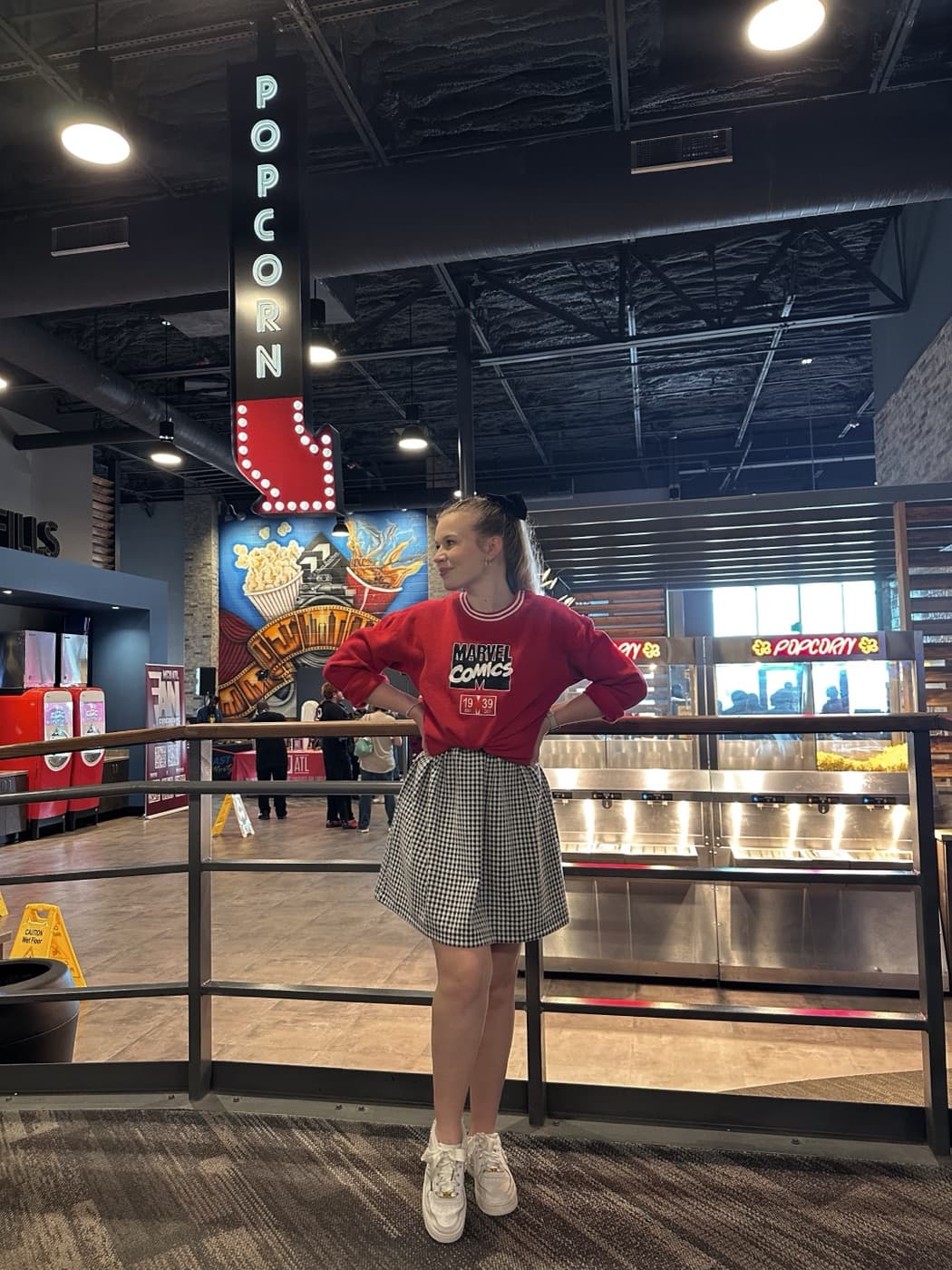 Kayla in a red top and gingham skirt in a theater lobby