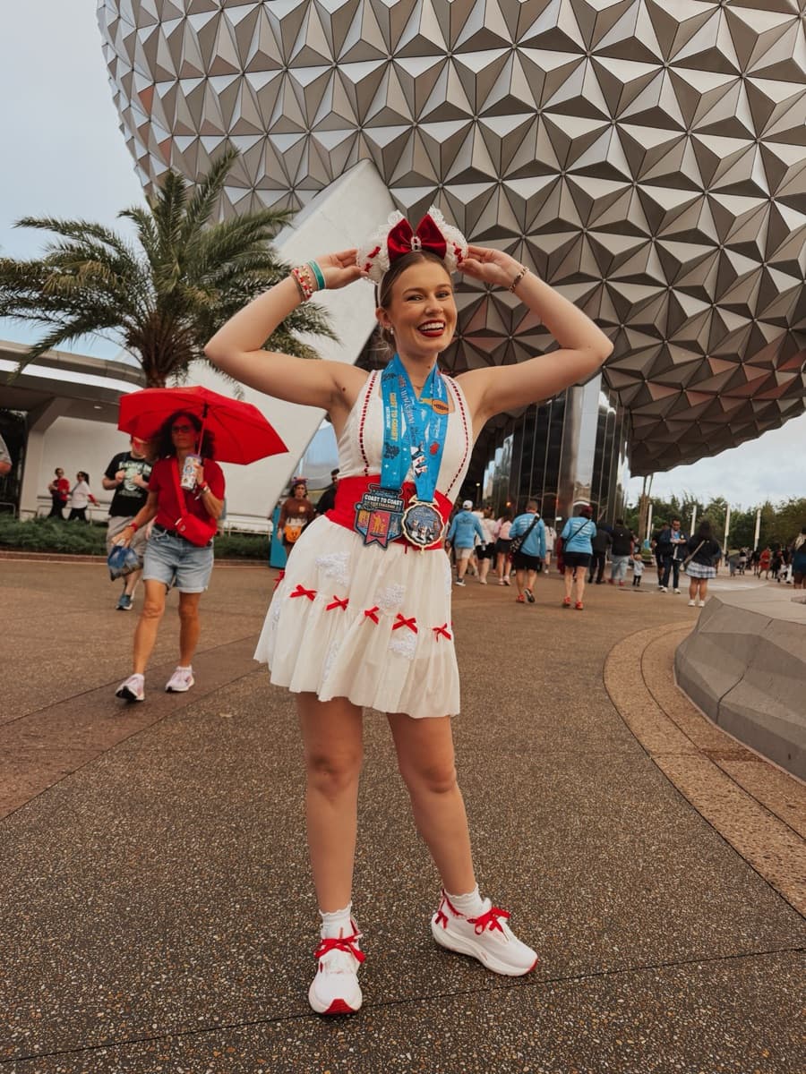 Kayla in a race costume holding up her medal in front of Spaceship Earth at Epcot